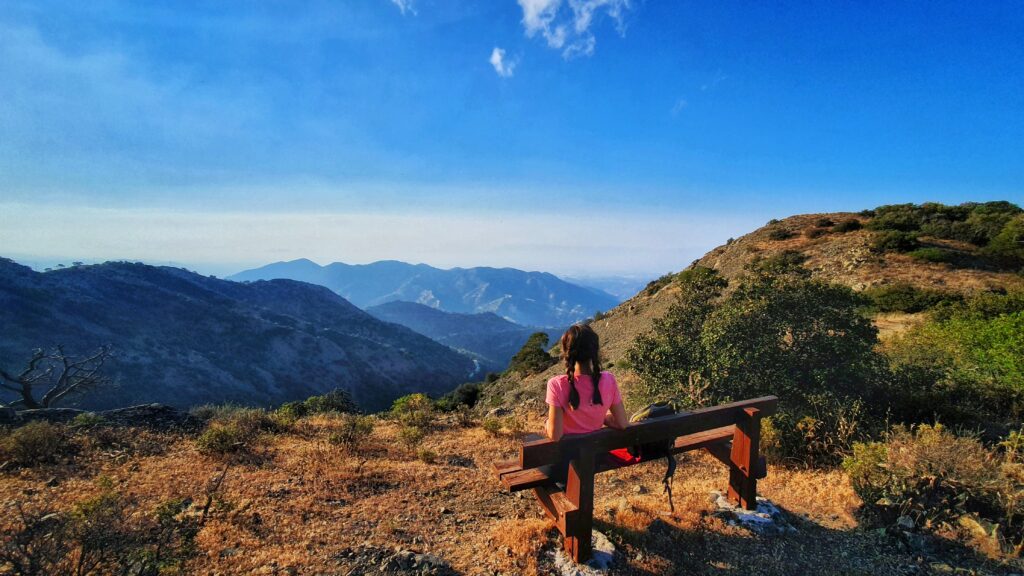Woman sitting on a wooden bench overlooking Cyprus mountains at sunset